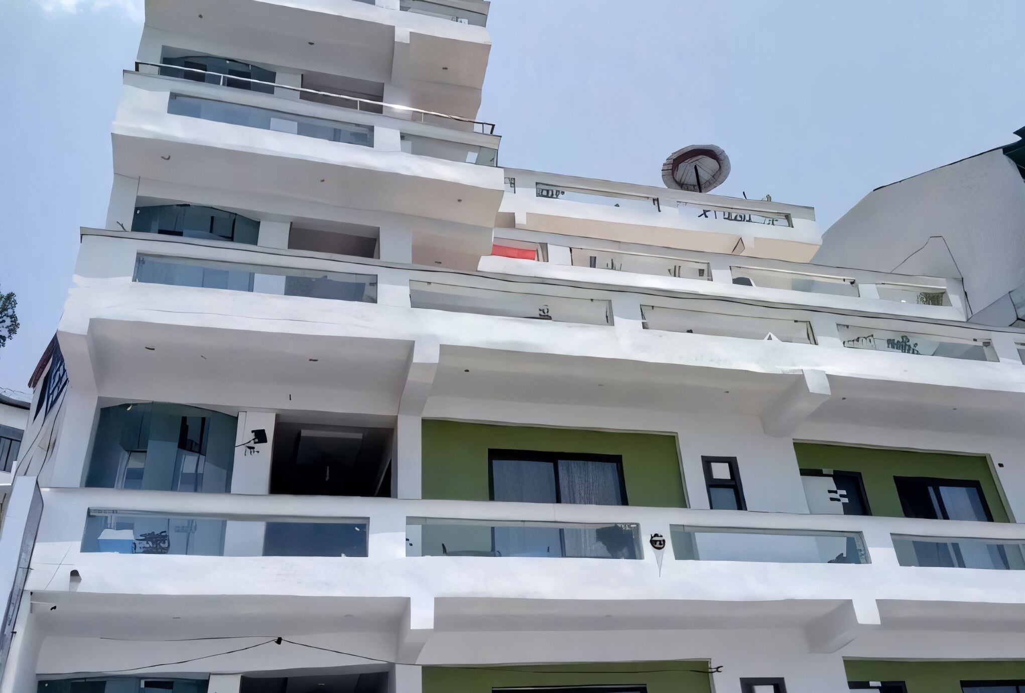 Un immeuble à plusieurs étages doté de balcons, de grandes fenêtres et d’un élément architectural circulaire distinctif sur le dernier étage.