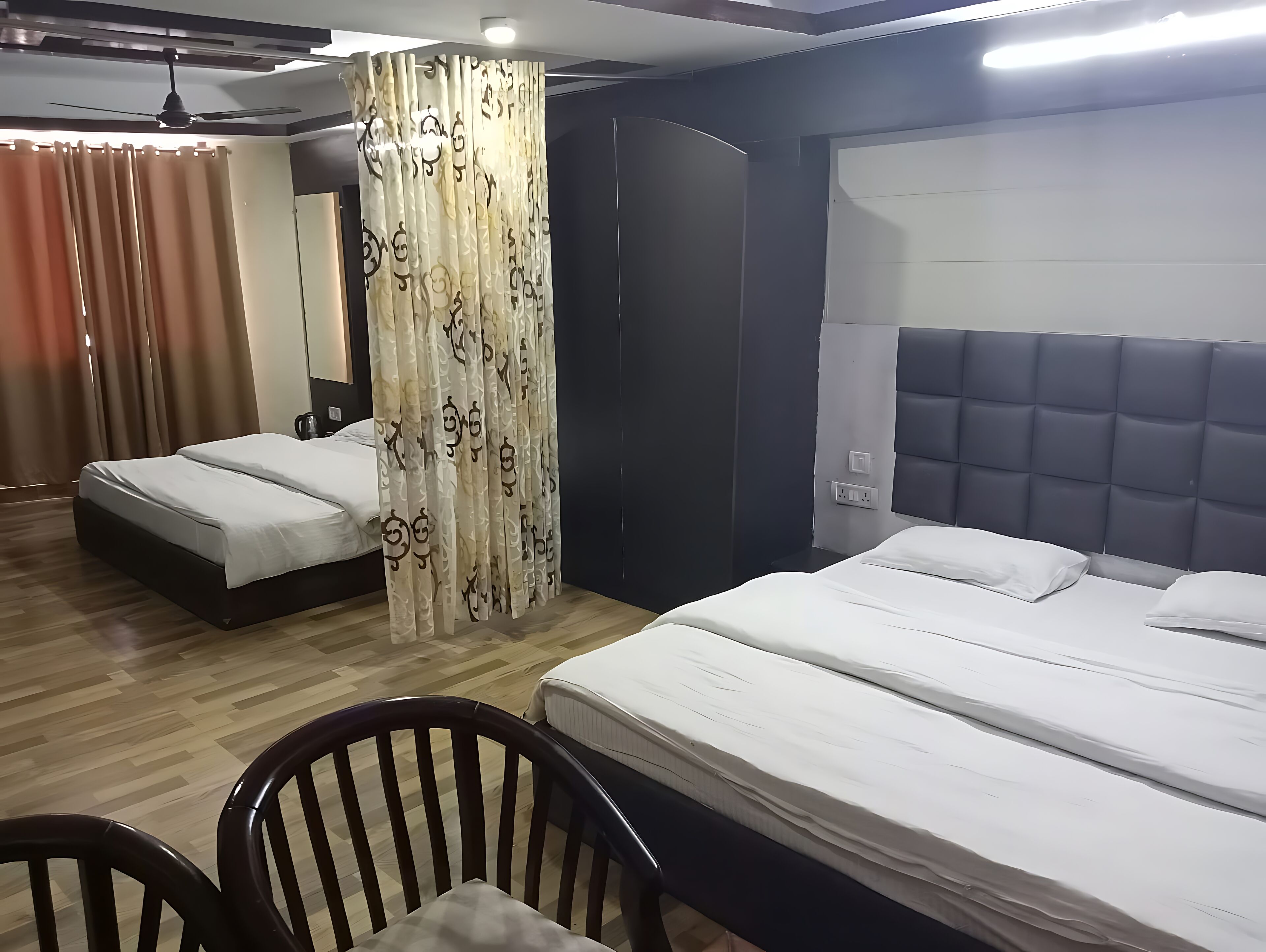 A hotel room with two beds, a wooden floor, a dark headboard, and a curtain with a pattern.