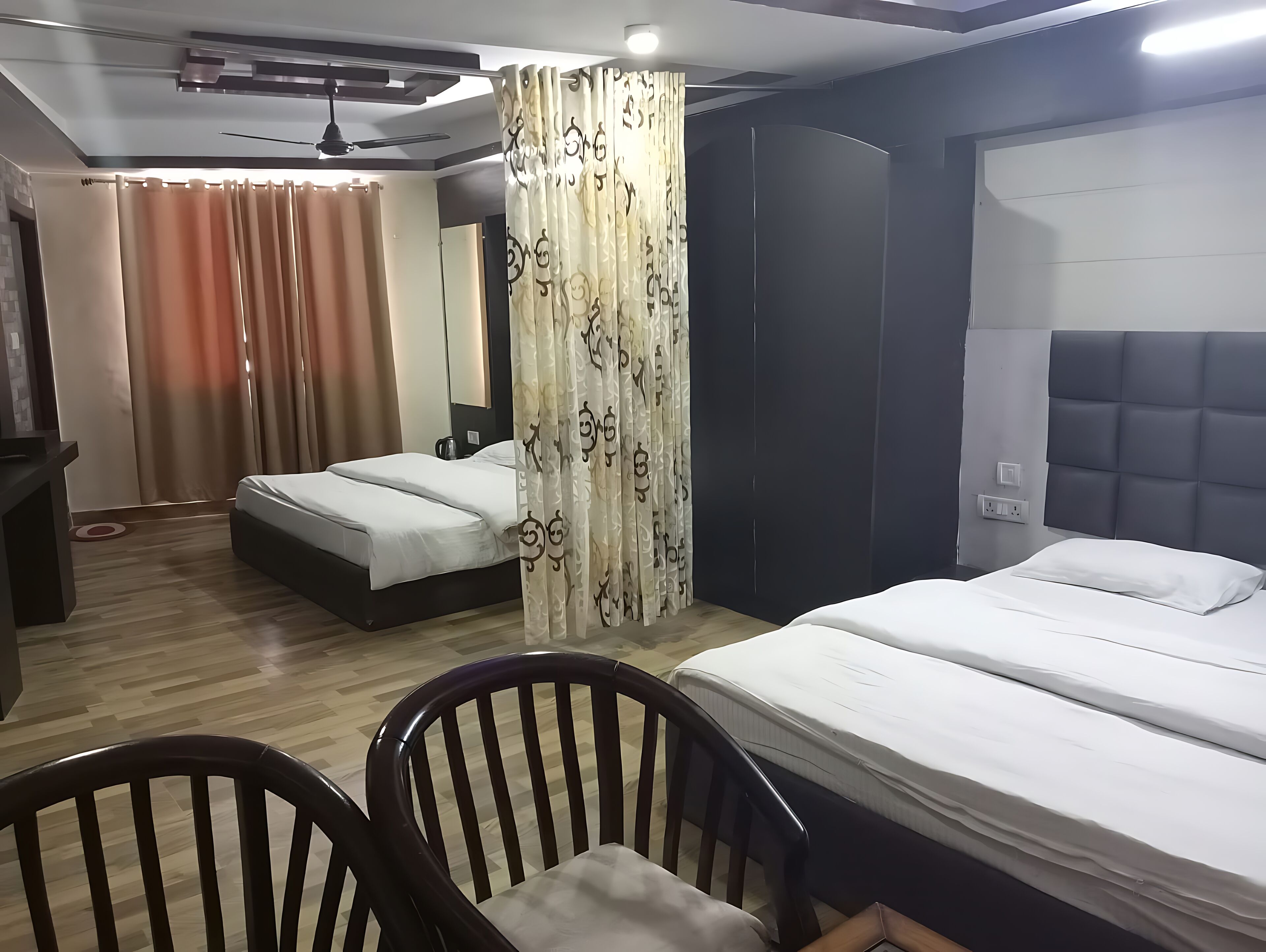 Habitación de hotel con dos camas, un escritorio, una silla, un armario y un ventilador de techo.