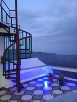 Una scala a chiocciola con ringhiera in metallo, che conduce a un balcone con pavimento in piastrelle e piante in vaso.