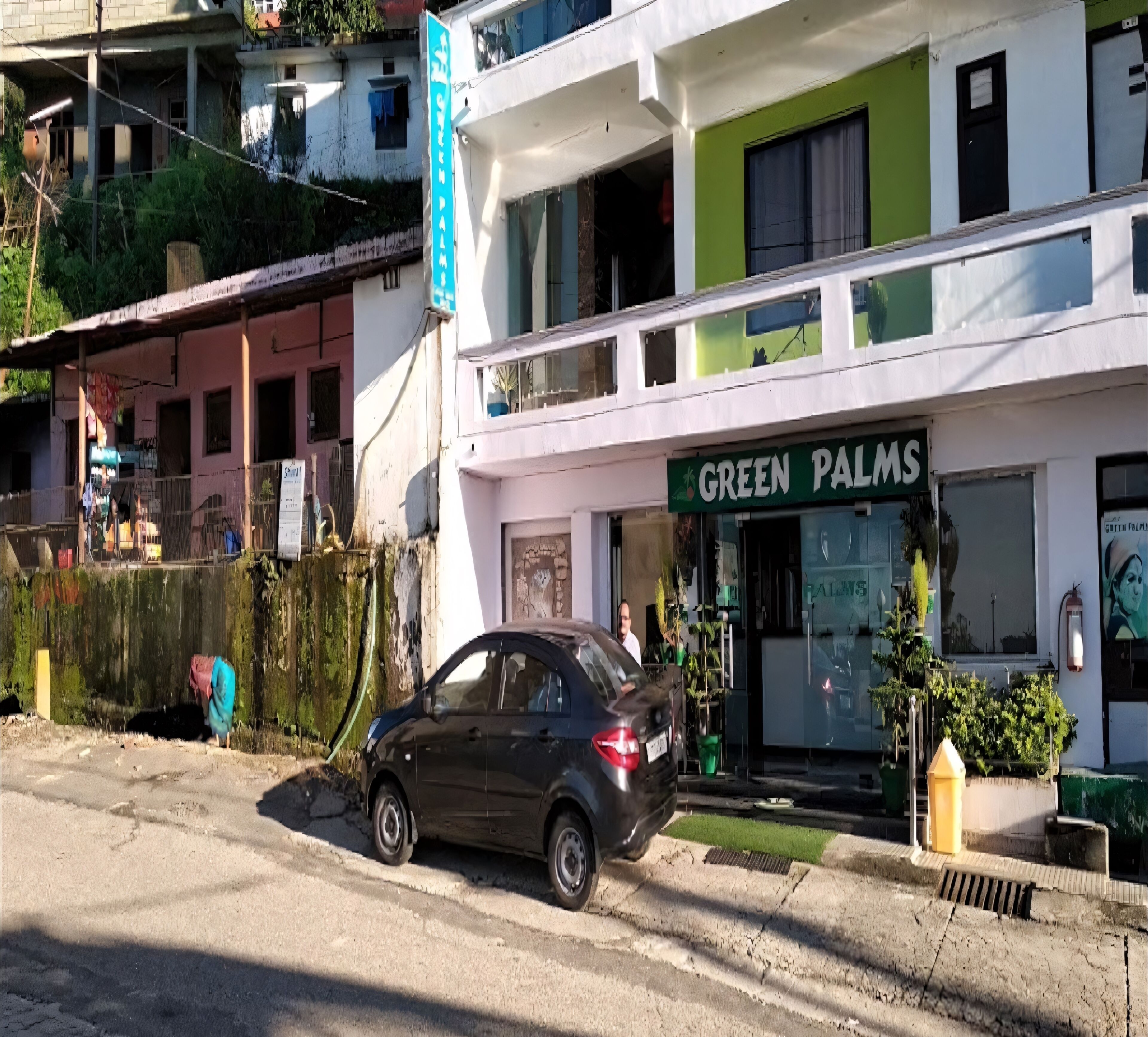 A building with a sign reading "GREEN PALMS" and a parked car in front.