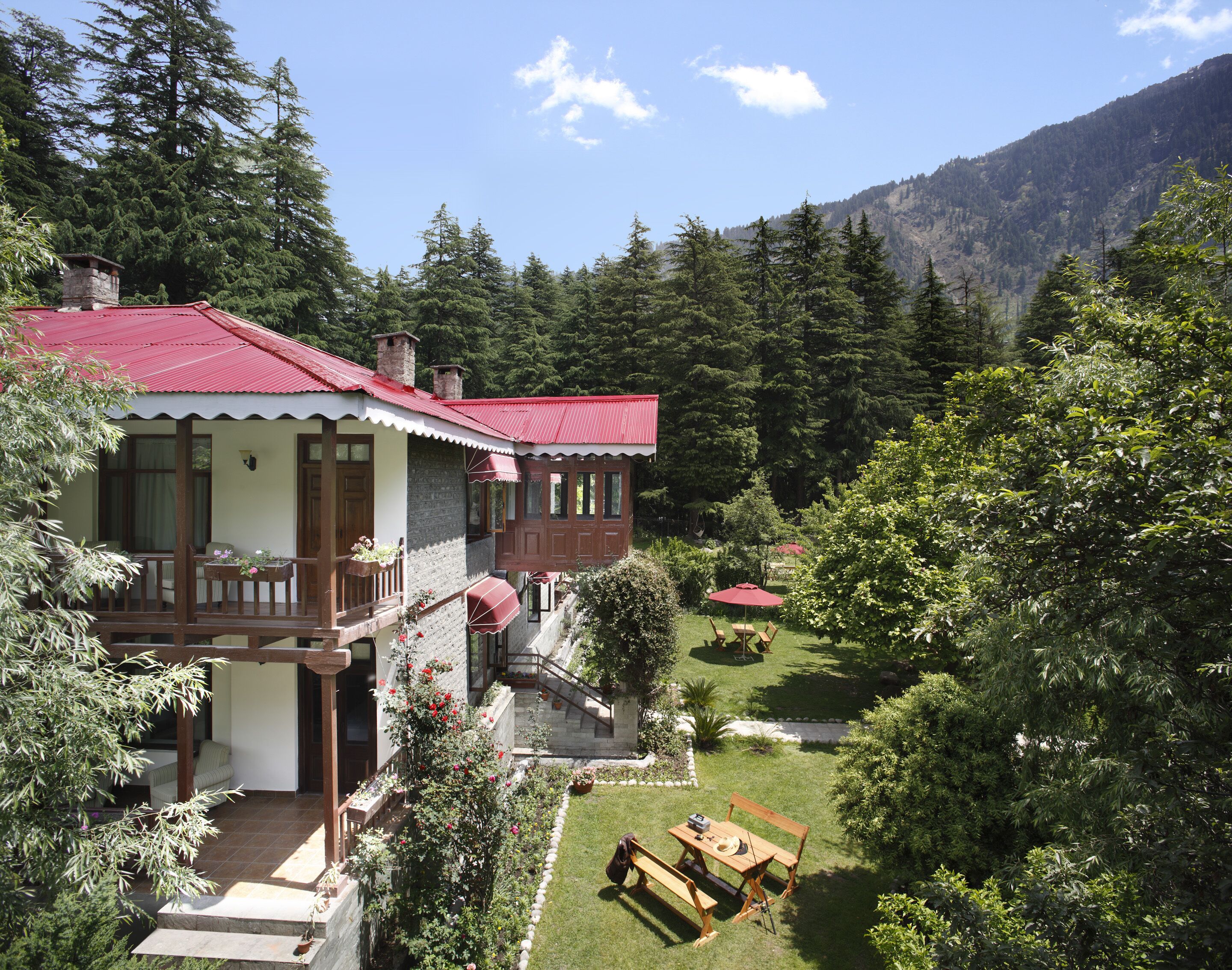Ein zweistöckiges Haus mit rotem Dach, einem Balkon und einem Garten mit Holztisch und -stühlen.