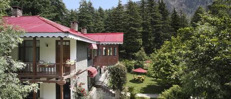 A two-story house with a red roof, a balcony, and a garden with a wooden table and chairs.