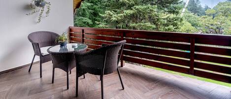 Una terraza de madera con una mesa y sillas, con vistas a una zona boscosa y una montaña al fondo.