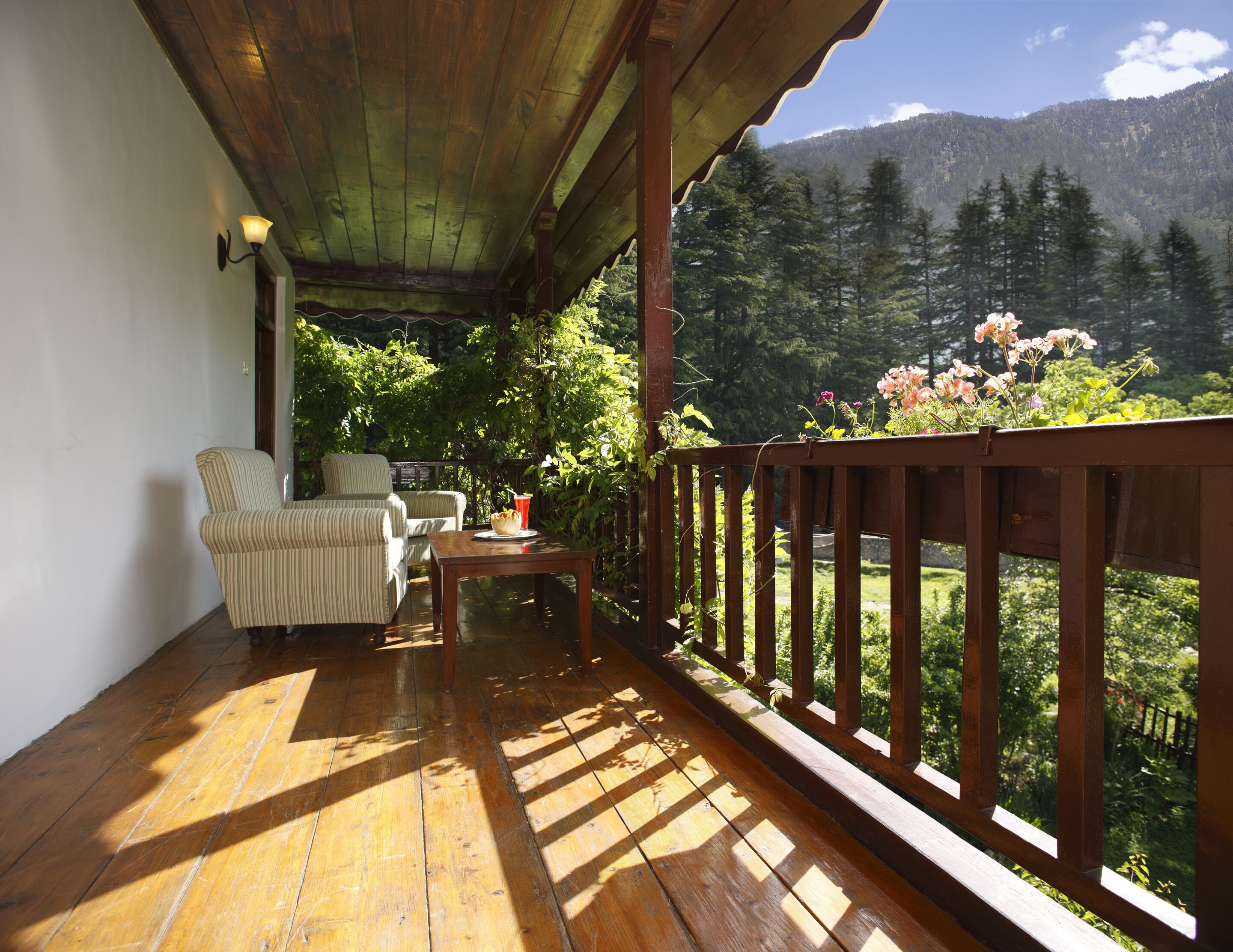 Un terrazzo in legno con vista su una foresta e montagne. Si vedono un tavolo e due sedie.