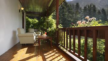 Terraza de madera con vistas a un bosque y montañas. Hay una mesa y dos sillas.
