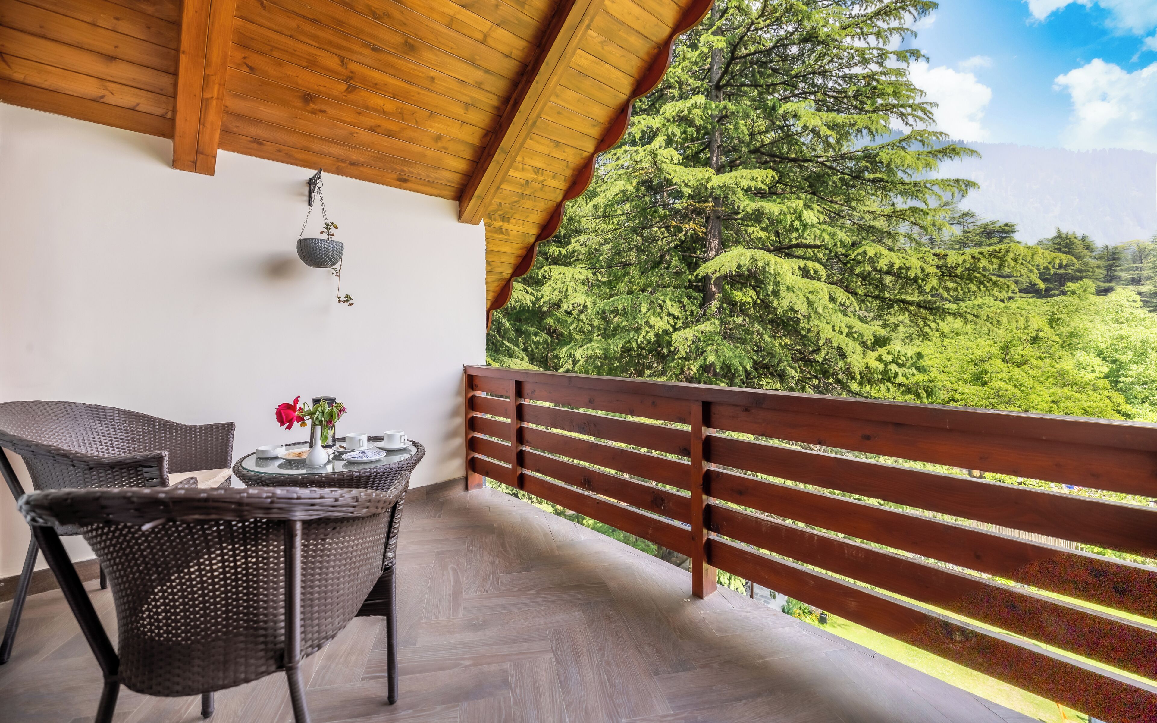 A balcony with wicker furniture, a hanging light fixture, and a view of a forested landscape.