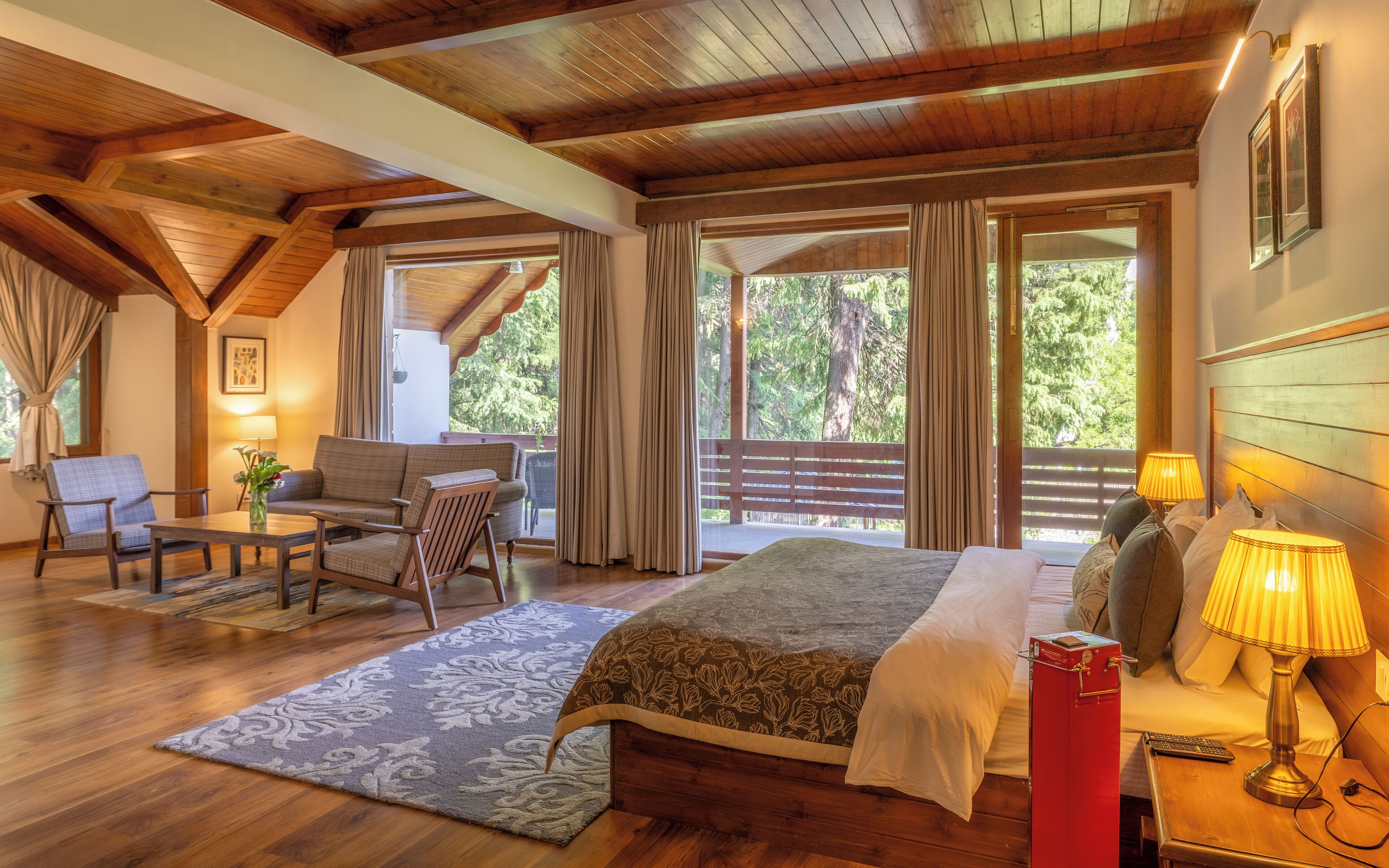 A spacious bedroom with a large bed, a sitting area with a sofa and chairs, and a view of the outdoors through large windows.