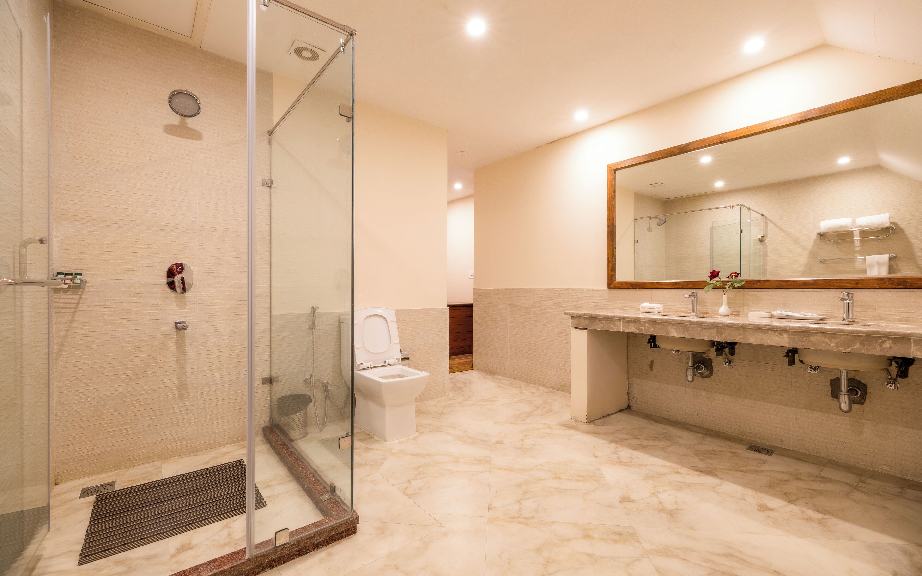 A modern bathroom with a glass-enclosed shower, a marble floor, a large mirror, and a sink with a vanity.