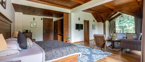 A spacious bedroom with a large bed, wooden ceiling beams, a television, and a view of the outdoors.