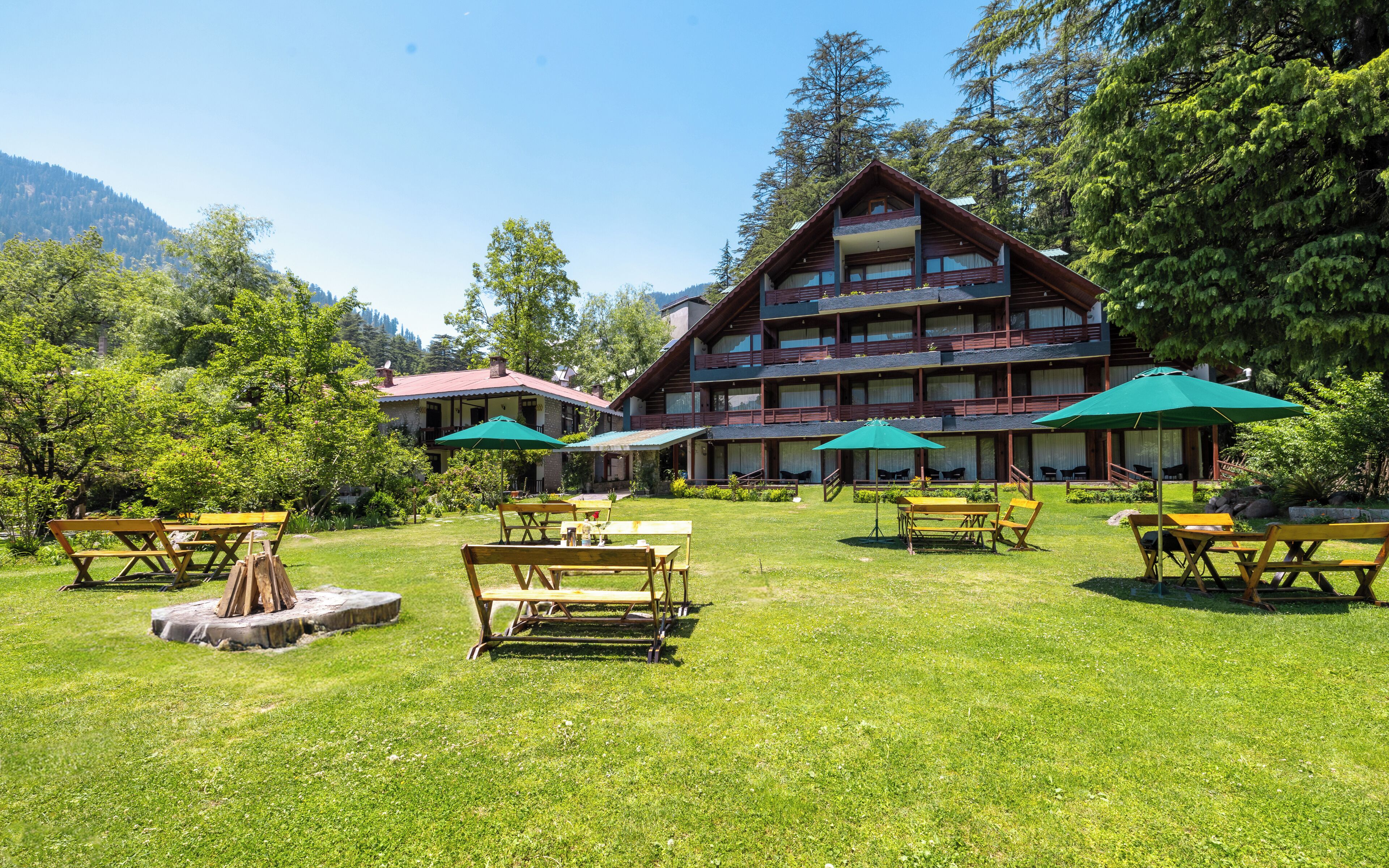 Una cabaña con un amplio patio al aire libre, varias mesas de comedor y sombrillas verdes.