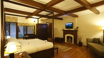 Een slaapkamer met een hemelbed, een televisie boven een open haard, en een zithoek met een bank en fauteuil.