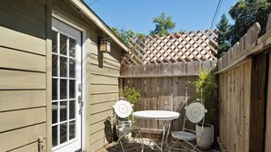 A patio with a wooden fence, a door, and a small table with chairs. - Charming Downtown Country Cottage (Chico)