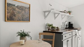 A kitchen with white cabinets, a wooden dining table, and a hanging painting. - Charming Downtown Country Cottage (Chico)