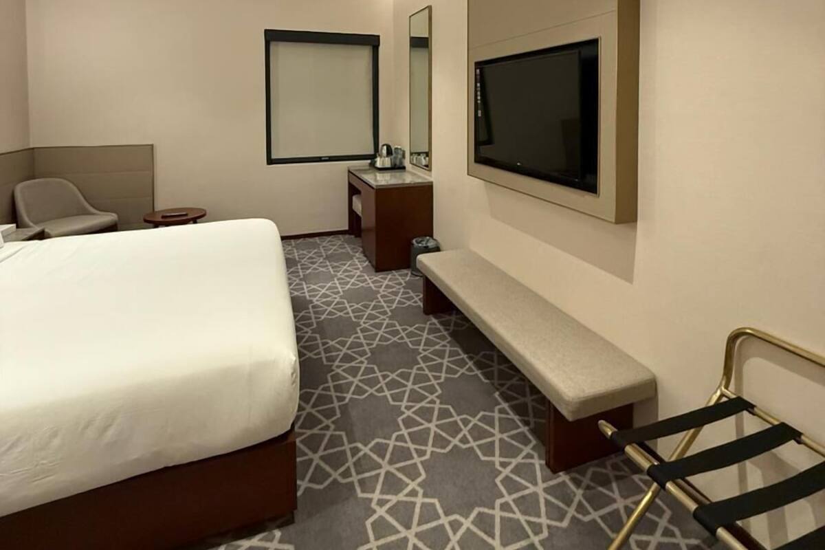 Ein modernes Hotelzimmer mit einem großen Bett, einem an der Wand montierten Fernseher, einem kleinen Schreibtisch und einer Bank.