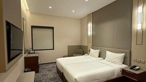 Hotellihuone, jossa on suuri sänky, yöpöydät, penkki, televisio ja kuviollinen matto.