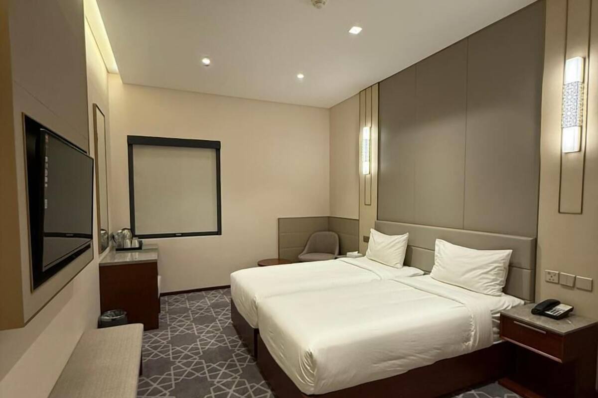 Ein Hotelzimmer mit einem großen Bett, Nachttischen, einer Bank, einem Fernseher und einem gemusterten Teppich.