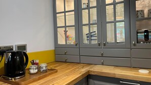 Une cuisine avec des meubles de couleur grise, un plan de travail en bois, une machine à café noire et une horloge.