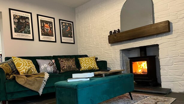 Un salon chaleureux avec un canapé vert, un pouf turquoise et une cheminée. Trois affiches encadrées sont accrochées au mur au-dessus de la cheminée.