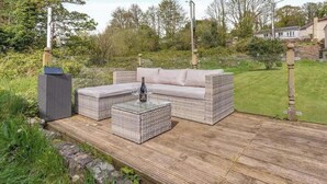 Une terrasse extérieure avec des meubles en osier, une table basse en verre et un verre à vin.