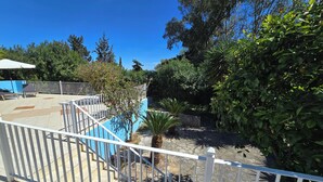 Una terraza con barandal blanco, piscina y follaje circundante.