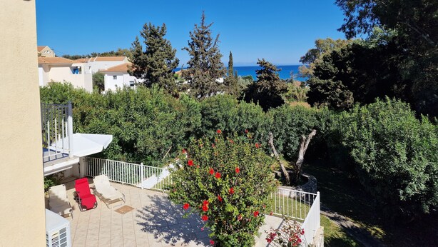 Una terraza con mobiliario exterior, vistas al mar y un jardín con árboles y arbustos.