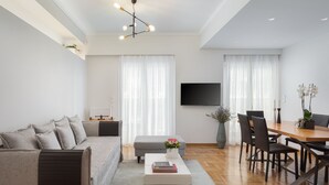 A modern living room with a sofa, coffee table, dining table, chairs, and a TV.