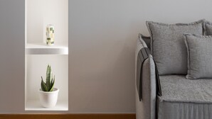 A minimalist room with a grey sofa, a white shelving unit with decorative items, and a grey wall.