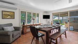 Un comedor con una mesa dispuesta para cuatro, un sofá y un televisor montado en la pared.