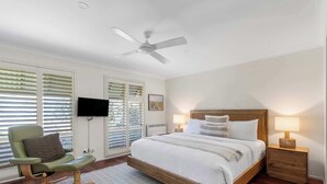 Un dormitorio con cama, una silla, un televisor, un ventilador de techo y una mesita de noche.