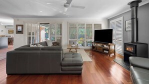 Una sala de estar moderna con un sofá modular, un televisor de pantalla plana, una chimenea y ventanas grandes con persianas.
