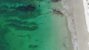 Vista aérea de una playa con agua turquesa cristalina y una orilla arenosa.