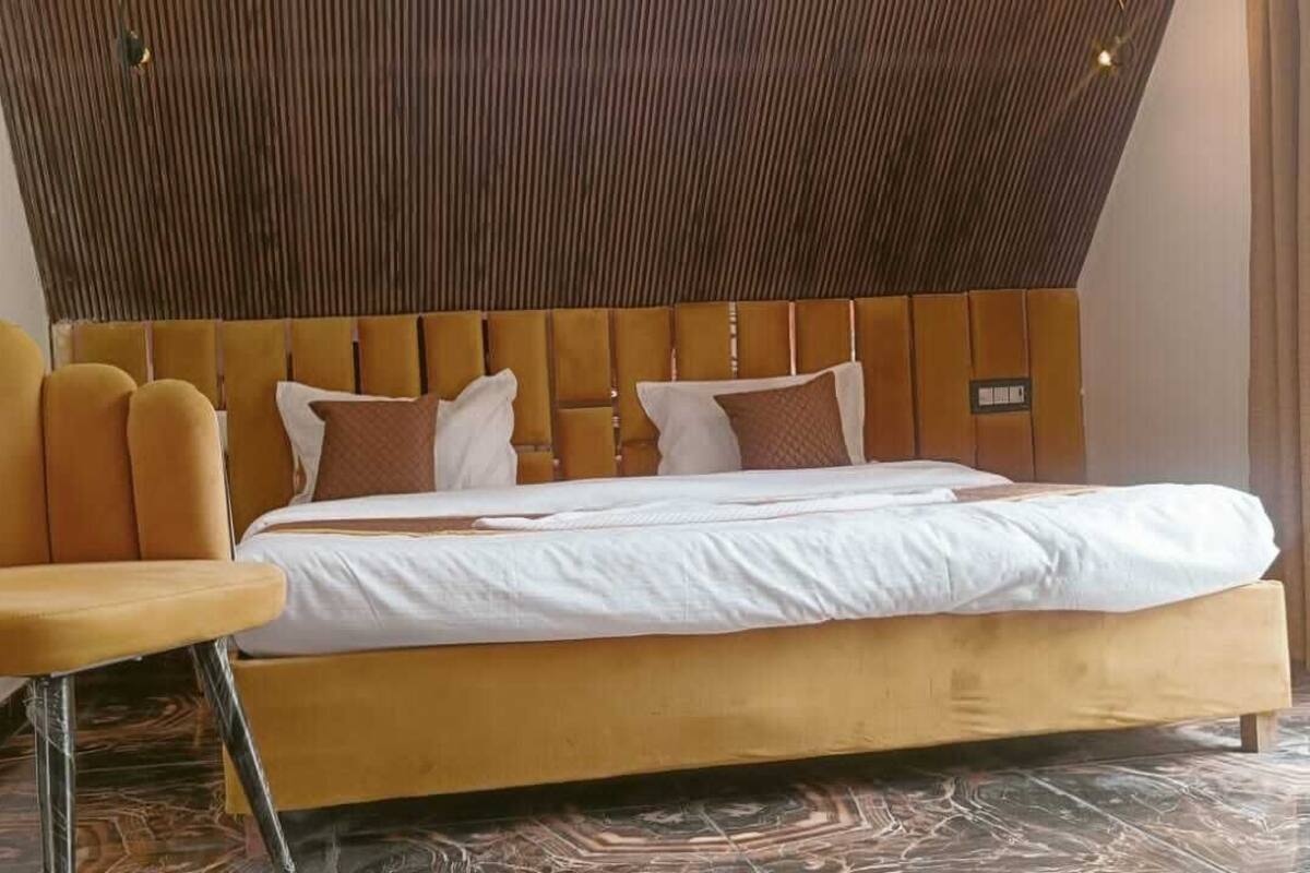 Ein modernes Schlafzimmer mit einem Holzkopfstück, einem gelb gepolsterten Sessel und einem großen Bett mit weißer Bettwäsche.