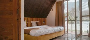 Un dormitorio con cabecera de madera, cama con ropa de cama blanca y vista a una valla blanca a través de una puerta de vidrio.