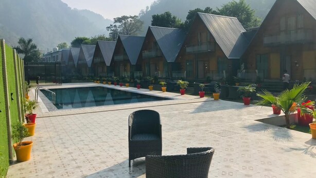 A pool area with a clear view of the pool, surrounded by potted plants and wicker chairs. - Eden Rock River Resort (Rishikesh)