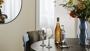 Une table à manger avec deux verres à vin, une bouteille de vin, une bouteille d’eau et un vase rempli de fleurs.