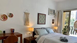 Ett sovrum med en säng, sänglampor, ett skrivbord, en stol och en balkong med en stol.