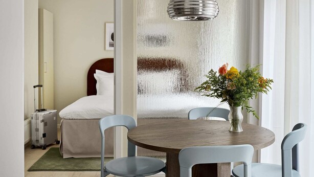 Een hotelkamer met een bed, een koffer, een eettafel met stoelen en een hanglamp.