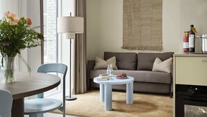 Un salon moderne comprenant un canapé, une table basse ronde, une table à manger avec des chaises, une lampe et un coin cuisine équipé d’appareils électroménagers.