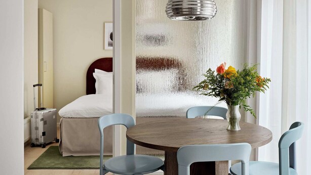 Ein Hotelzimmer mit einem Bett, einem Koffer, einem Esstisch mit Stühlen und einer Pendelleuchte.