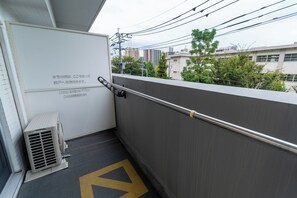 A narrow corridor with a metal handrail, a small air conditioning unit, and a yellow directional arrow on the floor. - vida hakata (Fukuoka)