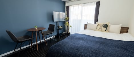 Quarto de hotel com uma cama grande, uma escrivaninha com cadeira, televisão e um vaso de plantas.