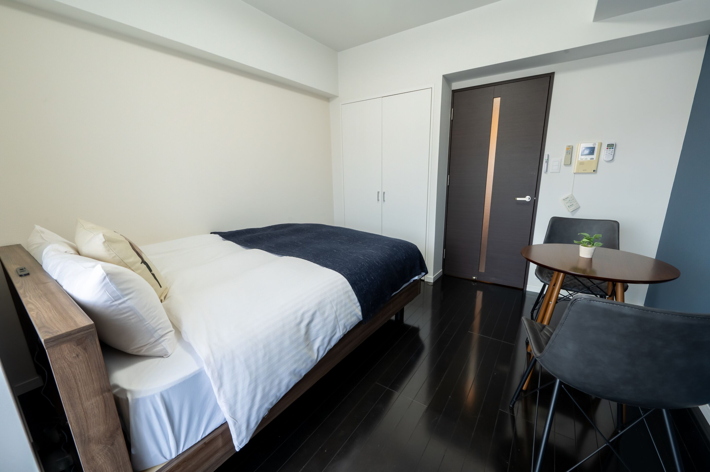 A modern hotel room with a large bed, a small table with a plant, and a chair.
