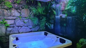 Un bain à remous dans une pièce avec un mur en pierre et une fresque représentant une cascade.