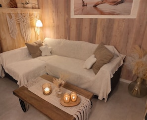 A cozy living room with a sectional sofa, a wooden coffee table with candles, and a wall-mounted lamp. - Gîte Maison de Campagne au nid D'ange Avec Jacuzzi (Saint-Michel-l'Observatoire)