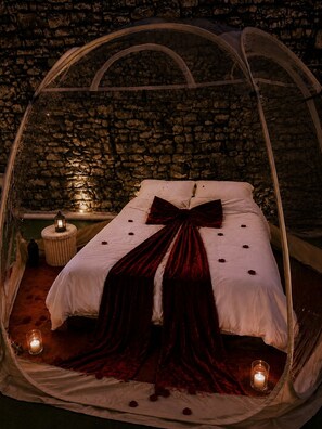 A tent-like room with a bed, candles, and a stone wall. - Gîte Maison de Campagne au nid D'ange Avec Jacuzzi (Saint-Michel-l'Observatoire)