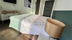 A bedroom with a bed, a bedside table, a lamp, a dresser, a TV, and an air conditioning unit. - Appartement Sole - Vue Splendide sur le Golfe de Porto-vecchio (Porto-Vecchio)