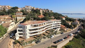 A multi-story building with balconies, situated on a coastal road with parked cars and a view of the sea. - Appartement Sole - Vue Splendide sur le Golfe de Porto-vecchio (Porto-Vecchio)