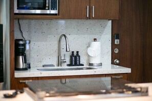 A kitchen with a stainless steel sink, a coffee maker, a soap dispenser, and a microwave above the counter.