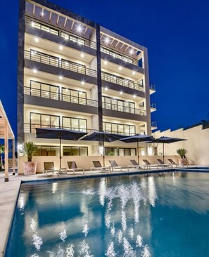A multi-story hotel with a swimming pool, outdoor seating, and a well-lit facade. - This brand-new 2-bedroom, 2-bath condo offers modern comfort with a stylish open layout and fully equipped kitchen. Enjoy a private rooftop terrace with outdoor kitchen and panoramic views—perfect for relaxing and taking in the beauty of Vista Mare. (Cabo San Lucas)